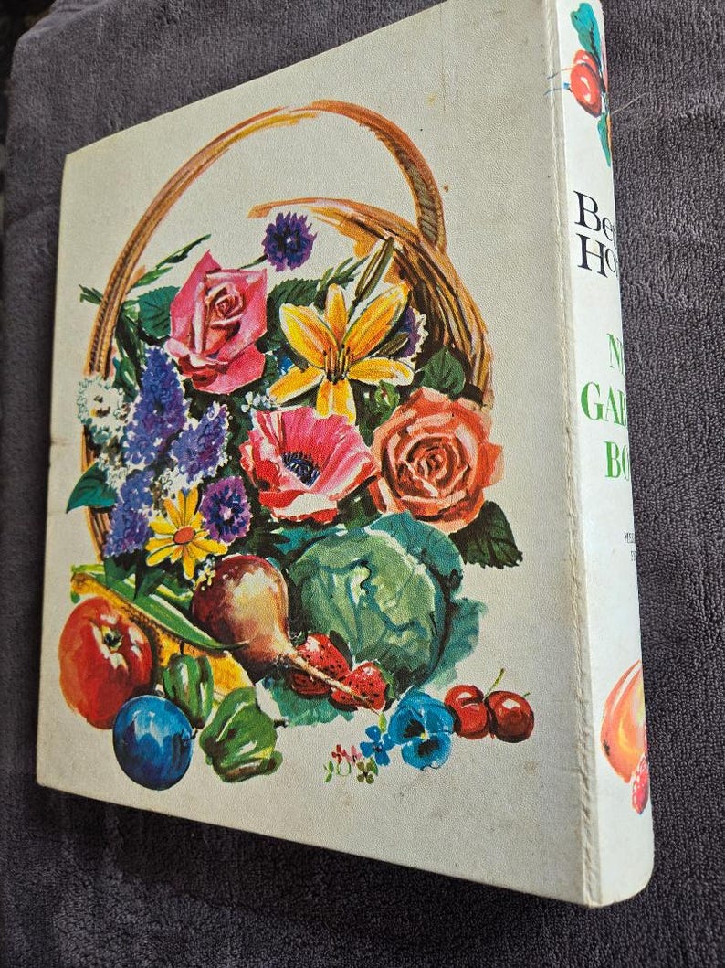 May include: A vintage gardening book with a colorful illustration of a basket overflowing with flowers, fruits, and vegetables. The cover features roses, poppies, and a cabbage. The spine displays the title "Better Homes and Gardens".