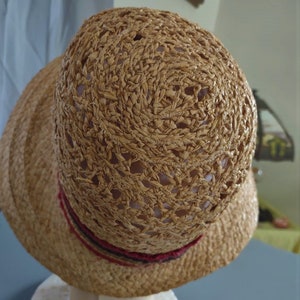 Puede incluir: Un sombrero de paja marr&oacute;n con un dise&ntilde;o tejido y una cinta roja y negra alrededor de la corona.
