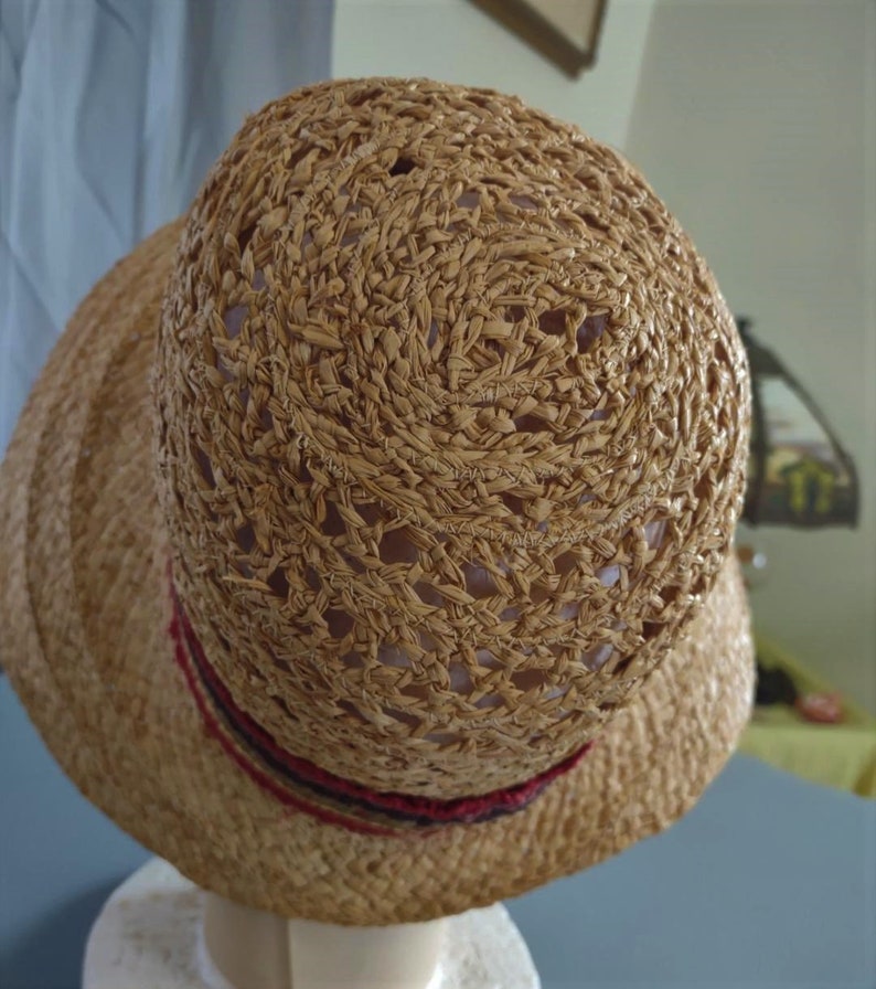 Puede incluir: Un sombrero de paja marr&oacute;n con un dise&ntilde;o tejido y una cinta roja y negra alrededor de la corona.