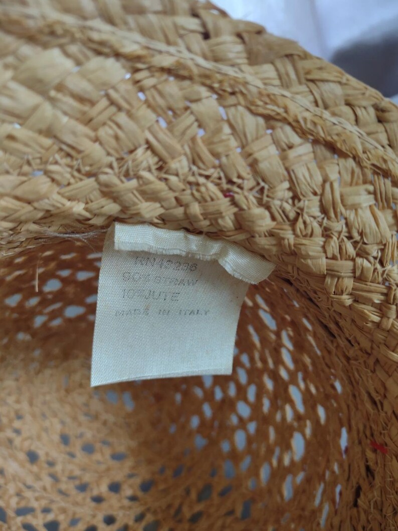 Puede incluir: Primer plano del interior de un sombrero de paja con una etiqueta blanca que dice "JN 42936 50% Straw 100% Italy Made in Italy".