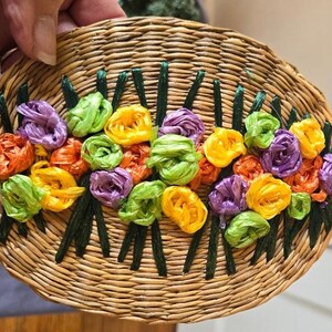 May include: A woven oval-shaped coaster with a design of colorful fabric flowers in shades of yellow, green, purple, and orange.