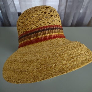 Puede incluir: Un sombrero de paja de ala ancha con un dise&ntilde;o tejido y una banda colorida de rojo, naranja, amarillo y marr&oacute;n.