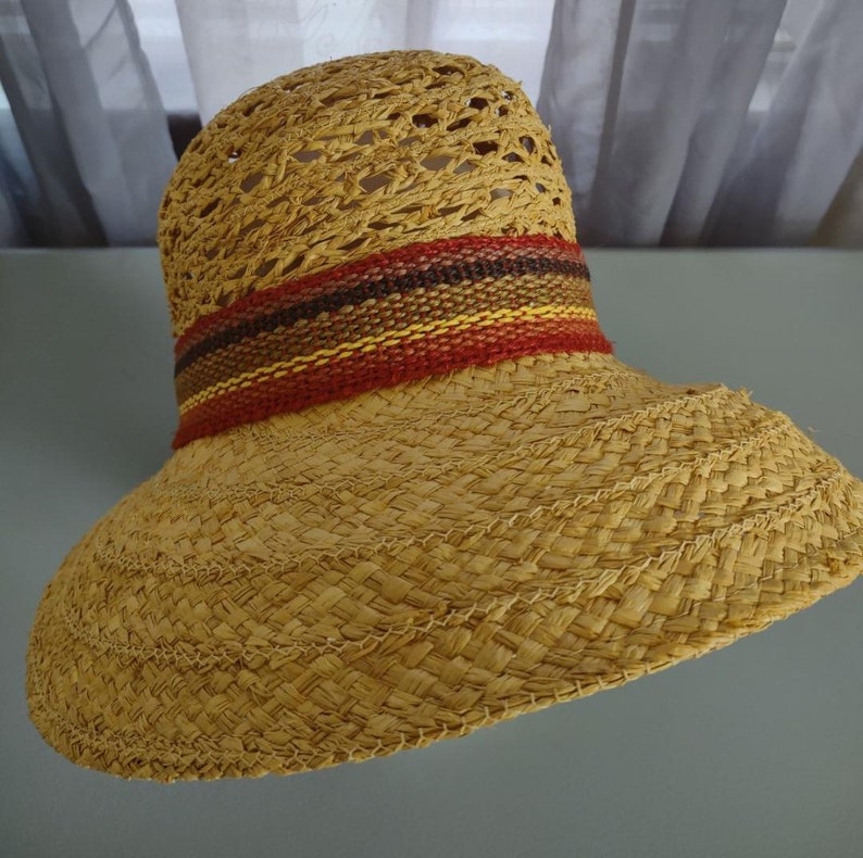 Puede incluir: Un sombrero de paja de ala ancha con un dise&ntilde;o tejido y una banda colorida de rojo, naranja, amarillo y marr&oacute;n.