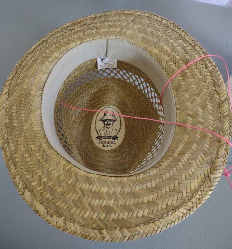 Peut inclure: Un chapeau de paille avec un motif tiss&eacute; brun. L'int&eacute;rieur du chapeau a une bande de tissu blanc avec une doublure en maille et une &eacute;tiquette qui indique "Original Panama Jack".