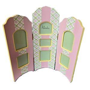 May include: A pink and green three-panel picture frame with a diamond pattern and yellow trim. The frame has five openings for pictures and the word "Watercolors" is written on the center panel.