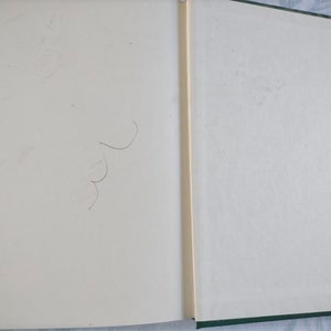 May include: A blank, white book with a green spine. The book is open to a blank page with a few faint pencil marks.