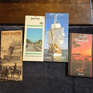May include: Four vintage travel guides: Fort Smith, New York, Virginia (1986-1987), and North Carolina (1973-74). The New York guide shows a highway scene, while Virginia features a sailing ship. The North Carolina guide has a sunset scene.