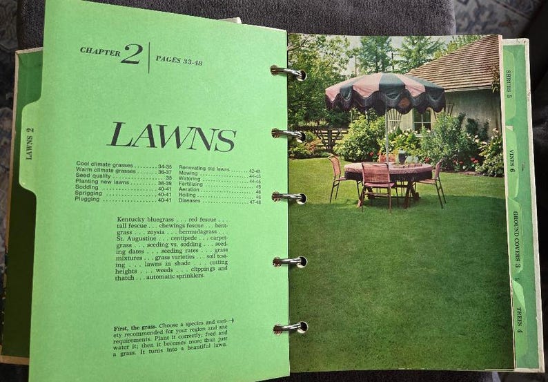 May include: Open book with a green cover and pages. The left page has the title "LAWNS" and a table of contents. The right page shows a color photo of a backyard with a table, chairs, and an umbrella.