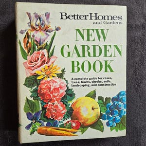 May include: A vintage "Better Homes and Gardens New Garden Book" with a floral illustration. The cover features a variety of colorful flowers, including roses, irises, and daisies, along with a yellow apple and grapes. The book's title is in large green letters.