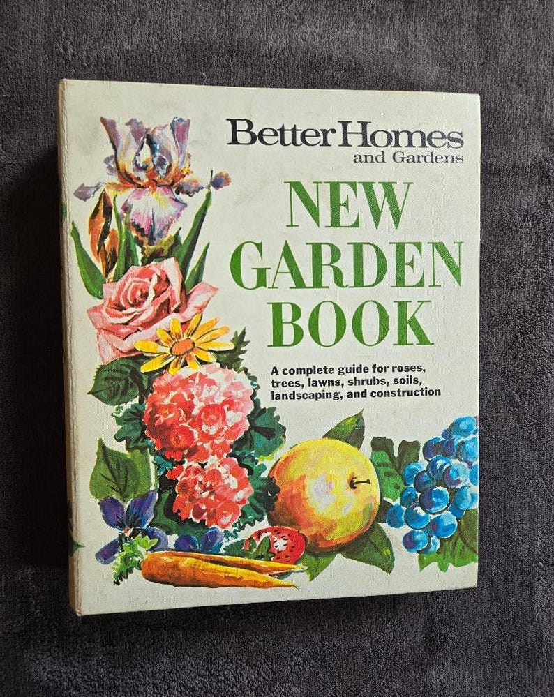 May include: A vintage "Better Homes and Gardens New Garden Book" with a floral illustration. The cover features a variety of colorful flowers, including roses, irises, and daisies, along with a yellow apple and grapes. The book's title is in large green letters.
