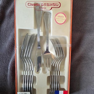 May include: A Claude Lebrun France boxed set containing six silver-toned fish knives and six fish forks. The cutlery features a beaded edge design. The orange box includes the brand name, a circular logo, and a label reading 6 fish forks and 6 fish knives Trianon.