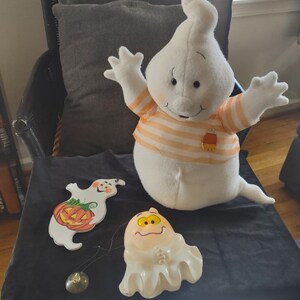 May include: Three plush ghost decorations for Halloween. One large white ghost with orange and white striped shirt and candy corn design. One small white ghost with a yellow face and one small white ghost with a pumpkin and a jack-o-lantern face.