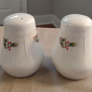 May include: A pair of white ceramic salt and pepper shakers with a holly and berry design.