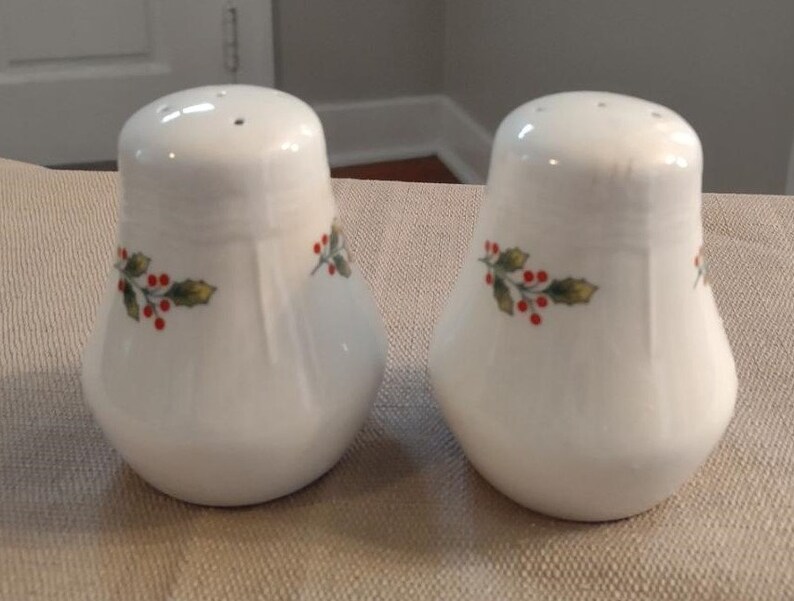 May include: A pair of white ceramic salt and pepper shakers with a holly and berry design.