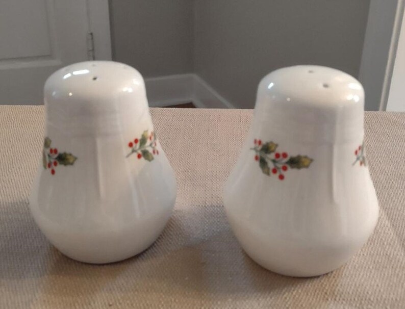 May include: Two white ceramic salt and pepper shakers with a holly and berry design.