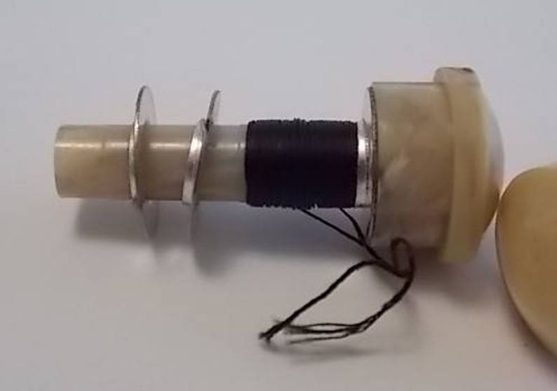 May include: A close-up of a white and black vintage sewing machine bobbin winder with a black thread spool and a white plastic base.