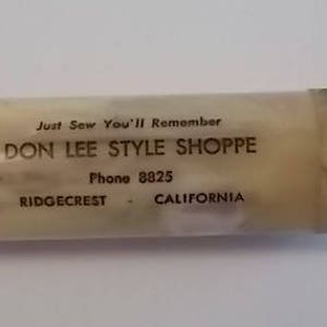 May include: A white plastic tube with the text "Just Sew You'll Remember Don Lee Style Shoppe Phone 8825 Ridgecrest - California" printed on it.