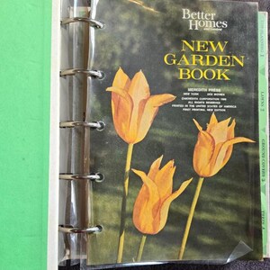 May include: A vintage "Better Homes and Gardens New Garden Book" with a cover featuring three orange tulips against a green and brown background. The book is in a binder with metal rings and a green spine.