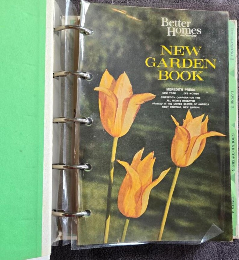 May include: A vintage "Better Homes and Gardens New Garden Book" with a cover featuring three orange tulips against a green and brown background. The book is in a binder with metal rings and a green spine.