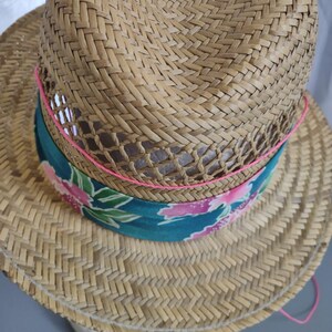 Peut inclure: Un chapeau de paille &agrave; large bord et un bandeau &agrave; motifs. Le bandeau est bleu sarcelle avec des motifs floraux roses et verts. Le chapeau est bord&eacute; d'un ruban rose.