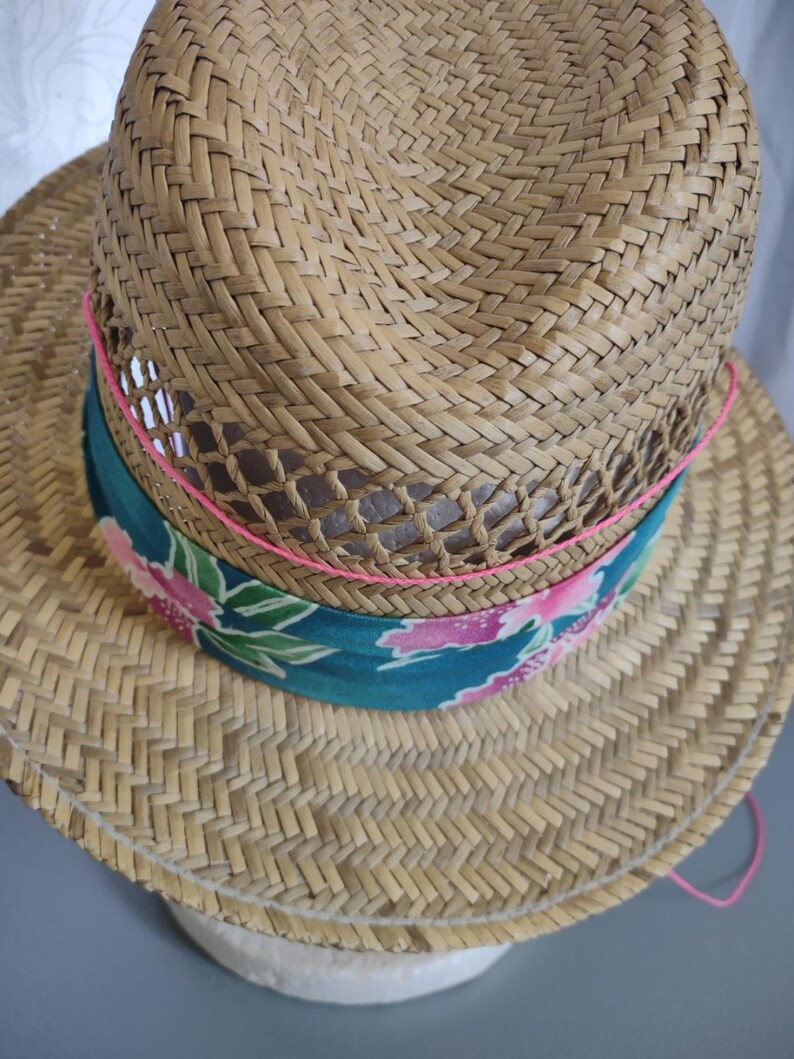 Peut inclure: Un chapeau de paille &agrave; large bord et un bandeau &agrave; motifs. Le bandeau est bleu sarcelle avec des motifs floraux roses et verts. Le chapeau est bord&eacute; d'un ruban rose.