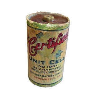 May include: Vintage Certified Unit Cell battery. The cylindrical battery has a brown top and a label with red and black text. The label reads "Unit Cell" and "Southern Battery Company, Appomattox, VA."