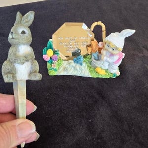 May include: A gray rabbit figurine with a white belly and a blue and white figurine of a girl holding a bucket of fish. The background is a blue and gold plaque with the text "For Blue of Stream and Blue of Sky I Give Thank You For Blessings".