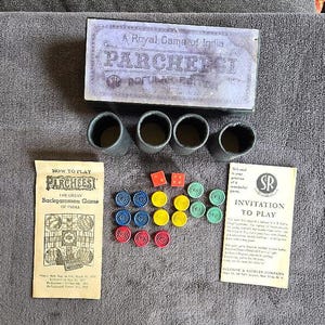 May include: A vintage Parcheesi board game set. The box is labeled "A Royal Game of India" and includes dice, game pieces in red, blue, yellow, and green, and instructions. The set also includes four gray dice cups.