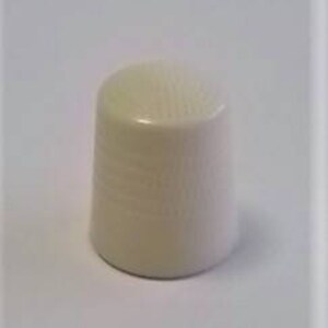 May include: A white ceramic thimble with a textured surface.