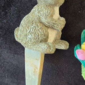 May include: A ceramic rabbit figurine with a white belly and brown fur. The rabbit is sitting on a green and white stake.