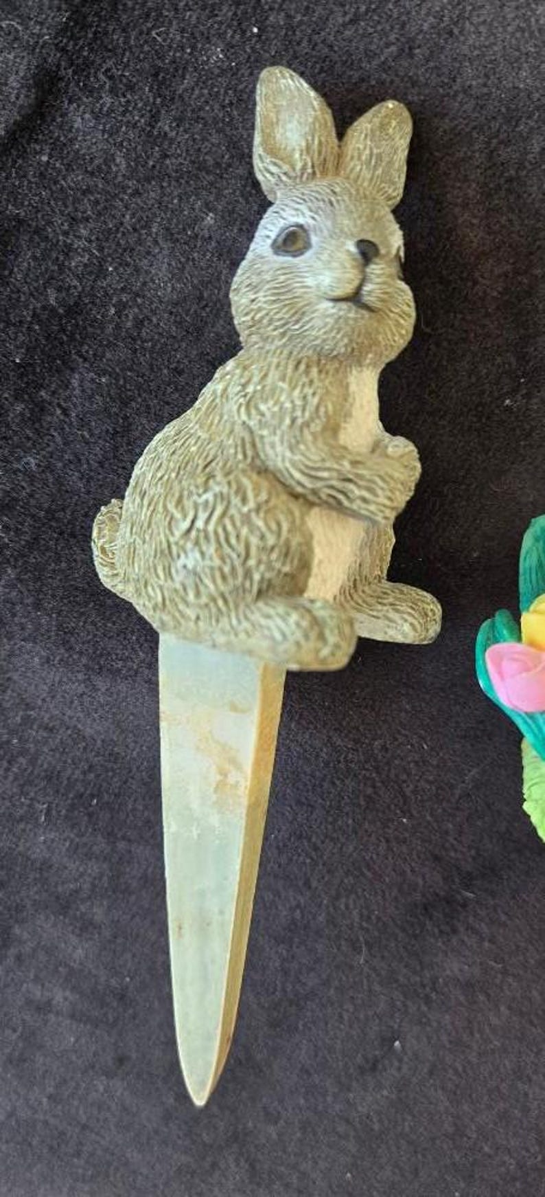 May include: A ceramic rabbit figurine with a white belly and brown fur. The rabbit is sitting on a green and white stake.