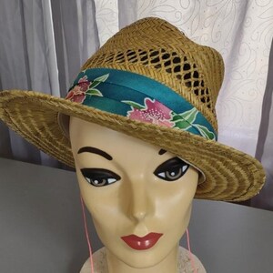 Peut inclure: Un chapeau de paille &agrave; large bord avec un ruban turquoise et floral. Le chapeau est fait de paille tress&eacute;e et a un design en maille.