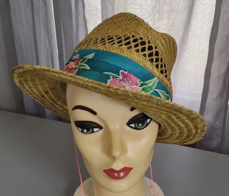 Peut inclure: Un chapeau de paille &agrave; large bord avec un ruban turquoise et floral. Le chapeau est fait de paille tress&eacute;e et a un design en maille.