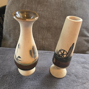 May include: Two ceramic vases with brown and white designs. The vase on the left has a floral design and the vase on the right has a wheel design.