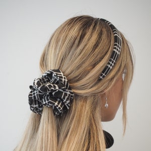 Puede incluir: Una diadema a cuadros en blanco y negro con un coletero a juego. La diadema se lleva en la cabeza de una persona y el coletero sujeta el pelo.