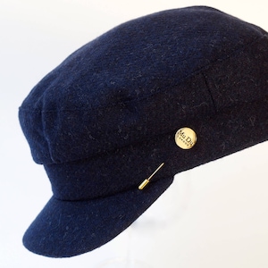 Peut inclure: Une casquette de newsboy en laine bleu foncé avec une épingle dorée qui dit "Mu Du London".
