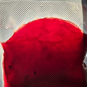 May include: A close-up of a red liquid inside a clear plastic bag with a textured surface.