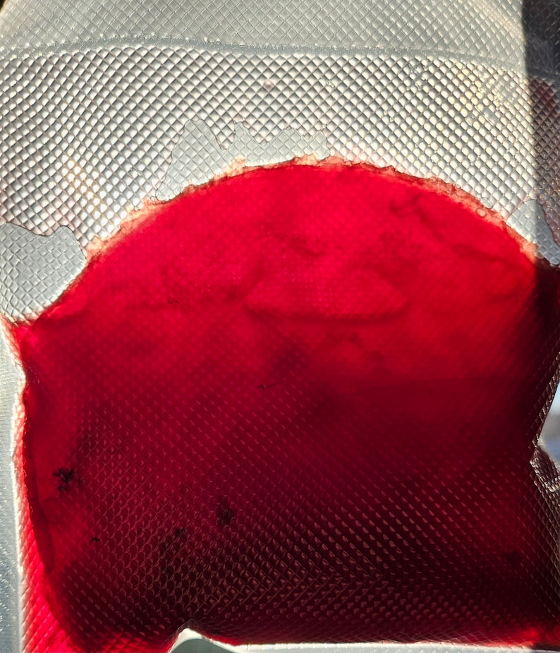 May include: A close-up of a red liquid inside a clear plastic bag with a textured surface.