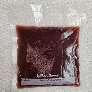 May include: A clear plastic bag with a red liquid inside. The bag has a label that says "FoodSaver" and "Contents/Contenu/Contenido:".
