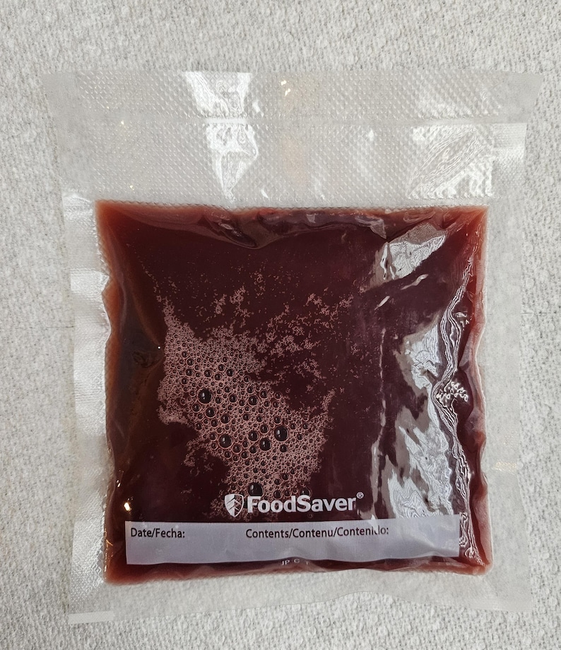 May include: A clear plastic bag with a red liquid inside. The bag has a label that says "FoodSaver" and "Contents/Contenu/Contenido:".