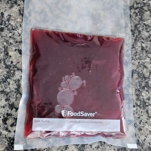 May include: A clear plastic bag with a red liquid inside. The bag has a label that says "FoodSaver" and "Contents/Contenu/Contenido: ".