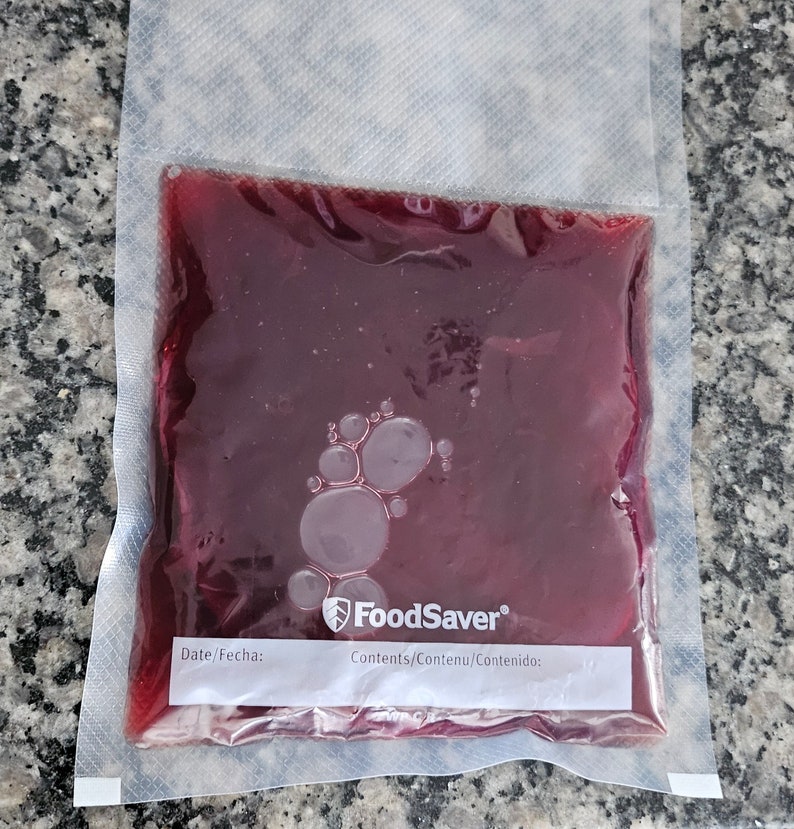 May include: A clear plastic bag with a red liquid inside. The bag has a label that says "FoodSaver" and "Contents/Contenu/Contenido: ".
