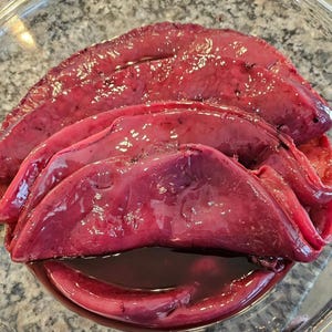 May include: A close-up of a bowl of raw, red beef liver. The liver is sliced and arranged in a bowl.