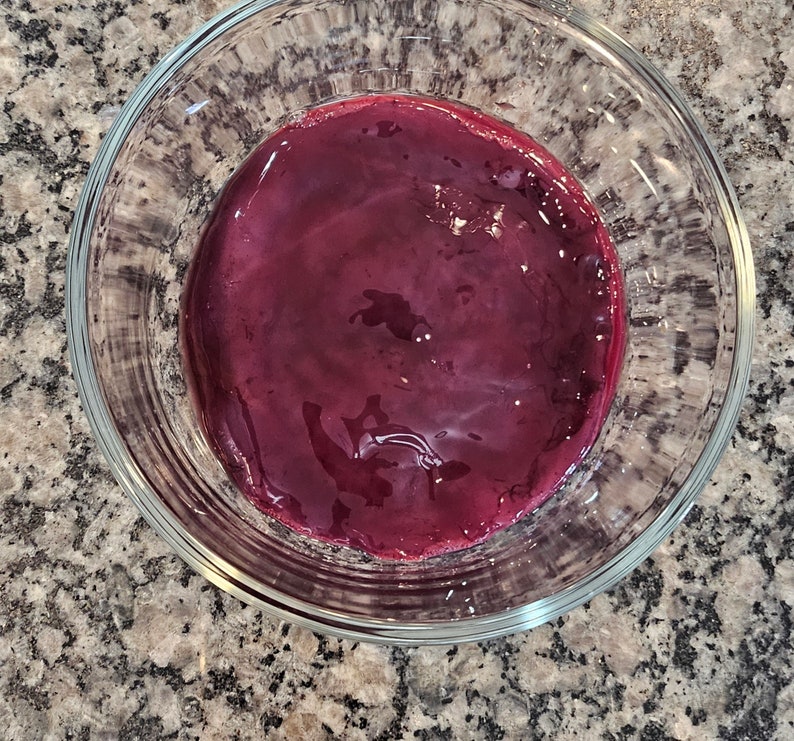 May include: A glass bowl filled with a deep red, almost purple, liquid. The liquid is smooth and glossy, reflecting light.