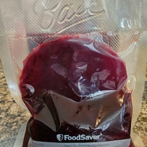 May include: A clear plastic bag with a red liquid inside. The bag is labeled "FoodSaver" and "Contents/Contenu/Contenido:".