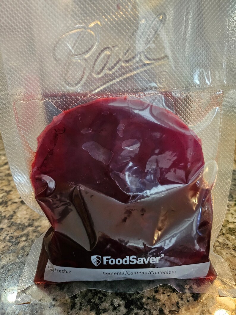May include: A clear plastic bag with a red liquid inside. The bag is labeled "FoodSaver" and "Contents/Contenu/Contenido:".