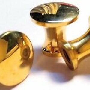 May include: Three gold-toned metal knobs with a screw thread on the back. The knobs have a round, slightly domed top and a flared base.