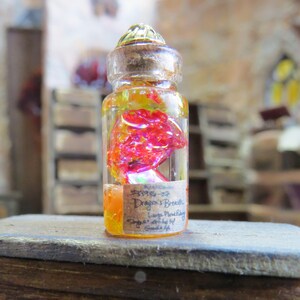 May include: A small glass bottle with a cork stopper and a label that reads "Dragon's Breath - Large Mouthful - Single Sniff At", filled with a red and yellow liquid.