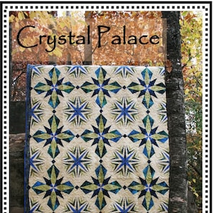 May include: A handmade quilt with a repeating starburst pattern in shades of blue, green, and cream. The quilt is displayed outdoors, with the text "Crystal Palace" and "Whirligig Designs" visible.