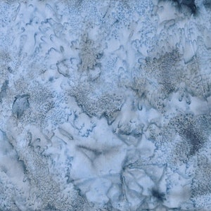 May include: A close-up view of a fabric with a mottled pattern in shades of blue and gray. The design has a watercolor-like effect, with areas of lighter blue blending into darker, textured patches. The overall effect is soft and organic.